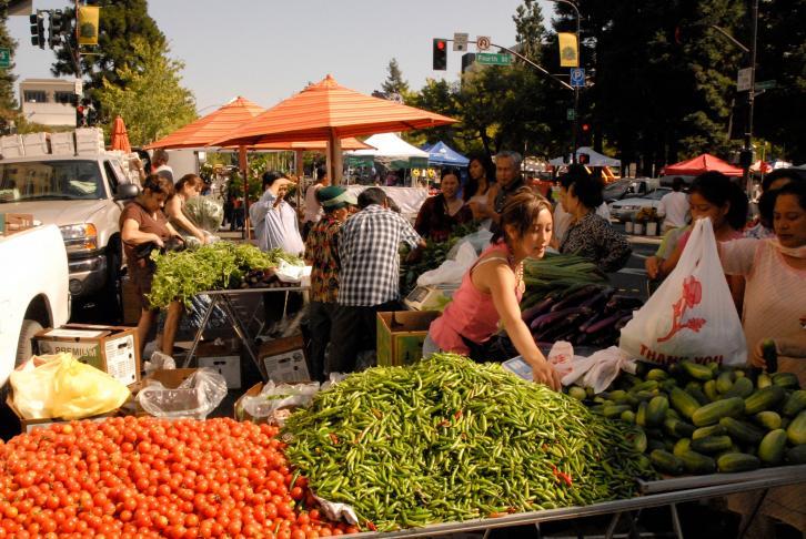 Residents shop at the Santa Rosa Farmers' Market, with piles of tomatoes, cucumbers and peppers in the foreground.